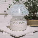 Mushroom candle lamp with white spots on clear glass. Filled with 100% soy wax on tile with bonsai in the background.