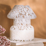 Mushroom candle lamp with white spots on clear glass. Filled with 100% soy wax on tile with dried flowers and tan background.