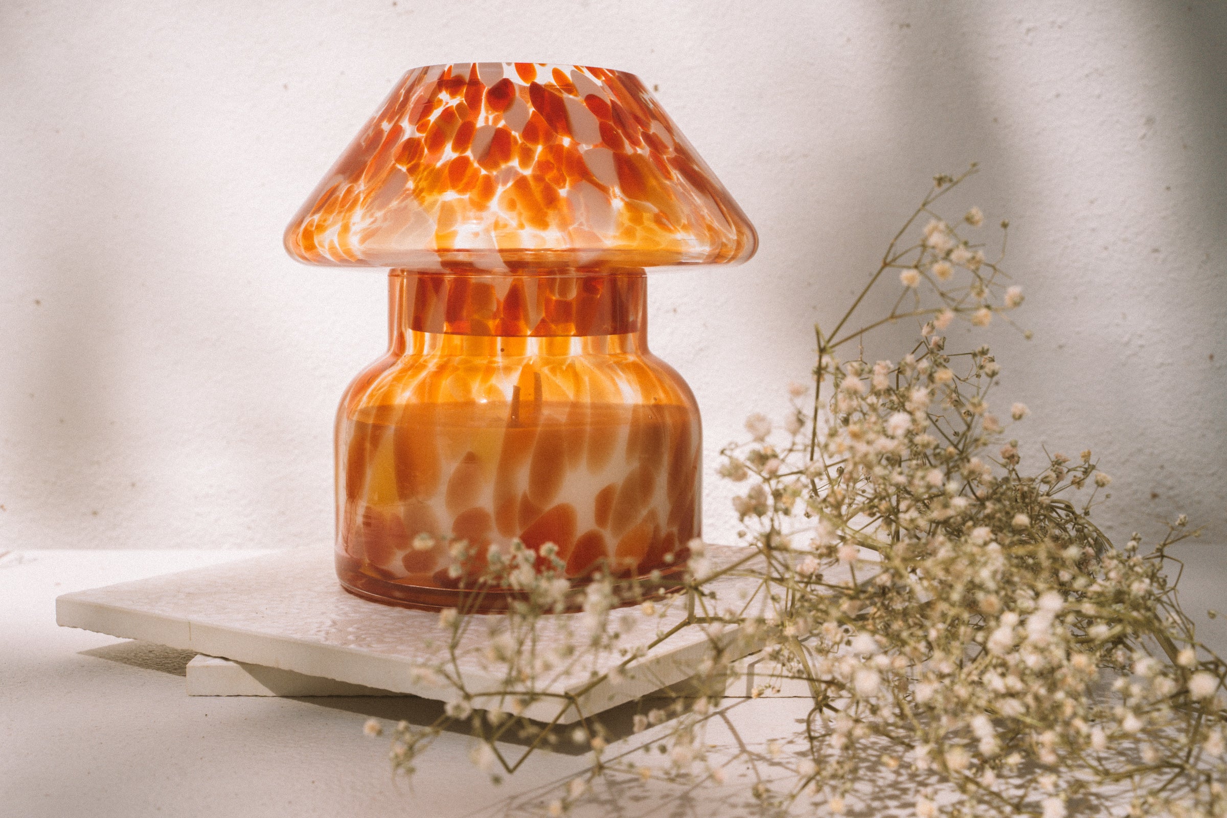 Mushroom candle lamp with red, orange and white spots on clear glass. Retro lamp is filled with 100% soy wax placed one white tiles with dried flowers.