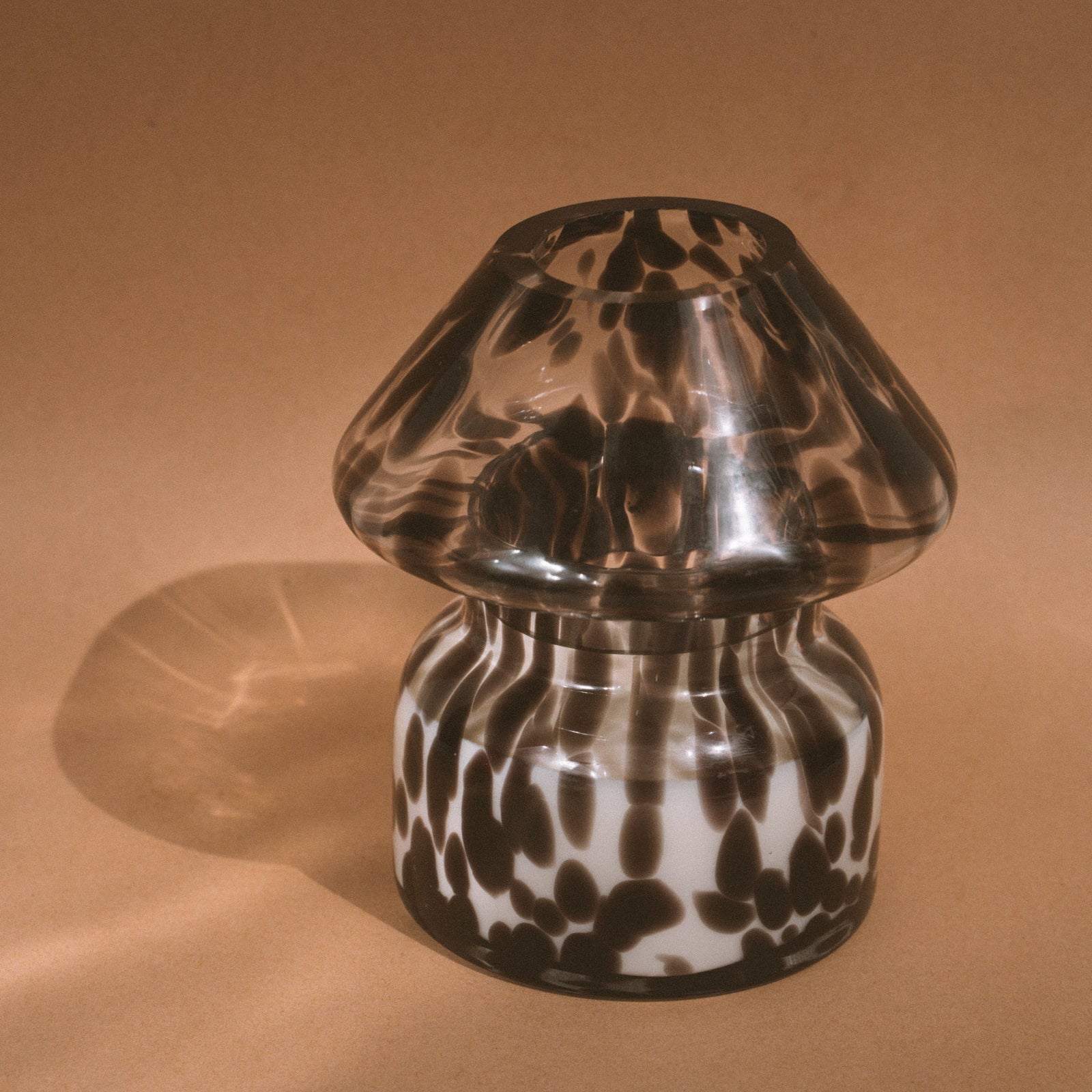 Dalmation spotted black glass mushroom candle lamp. Filled with 100% soy wax on tan background with sun reflection.