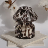 Dalmation spotted black glass mushroom candle lamp. Candle lamp is sitting on tile with cotton in the background