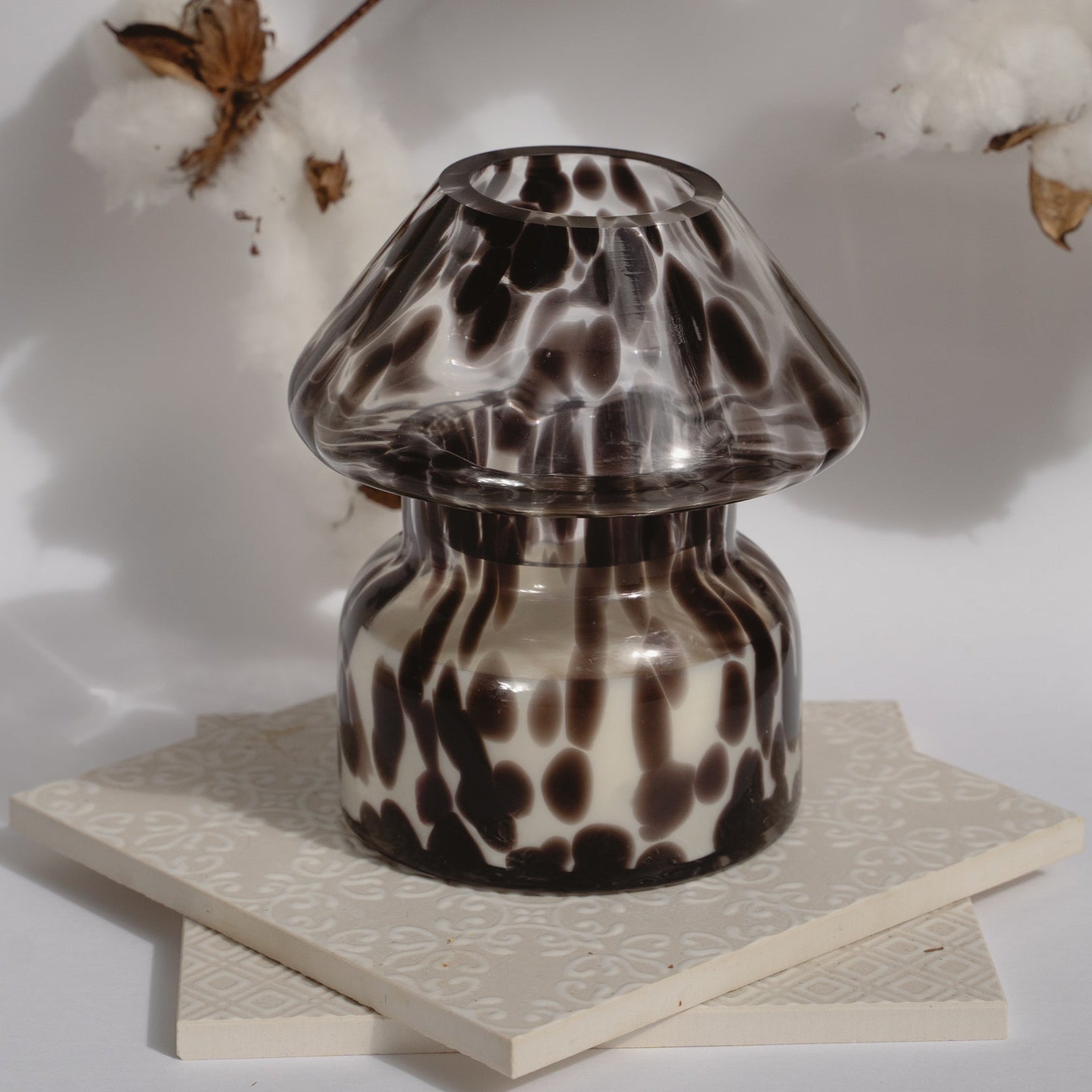 Dalmation spotted black glass mushroom candle lamp. Candle lamp is sitting on tile with cotton in the background