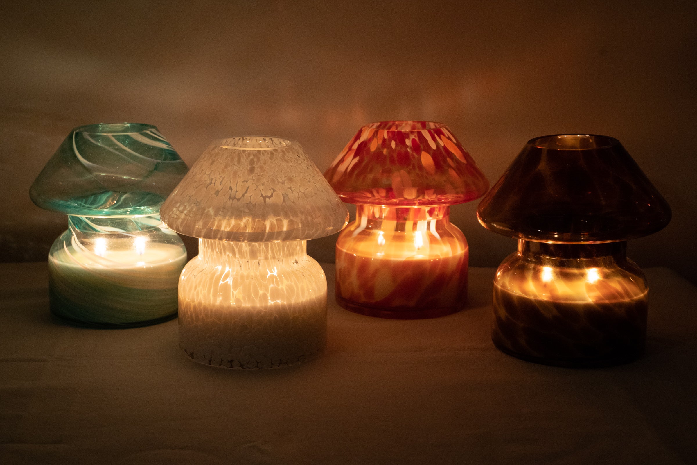 Mushroom candle lamp with light and dark brown spots on tan coloured glass. Leopard candle lamp is lit next to 3 other coloured lit mushroom lamps.