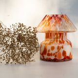 Mushroom candle lamp with red, orange and white spots on clear glass. Retro lamp is filled with 100% soy wax placed next to dried flowers.