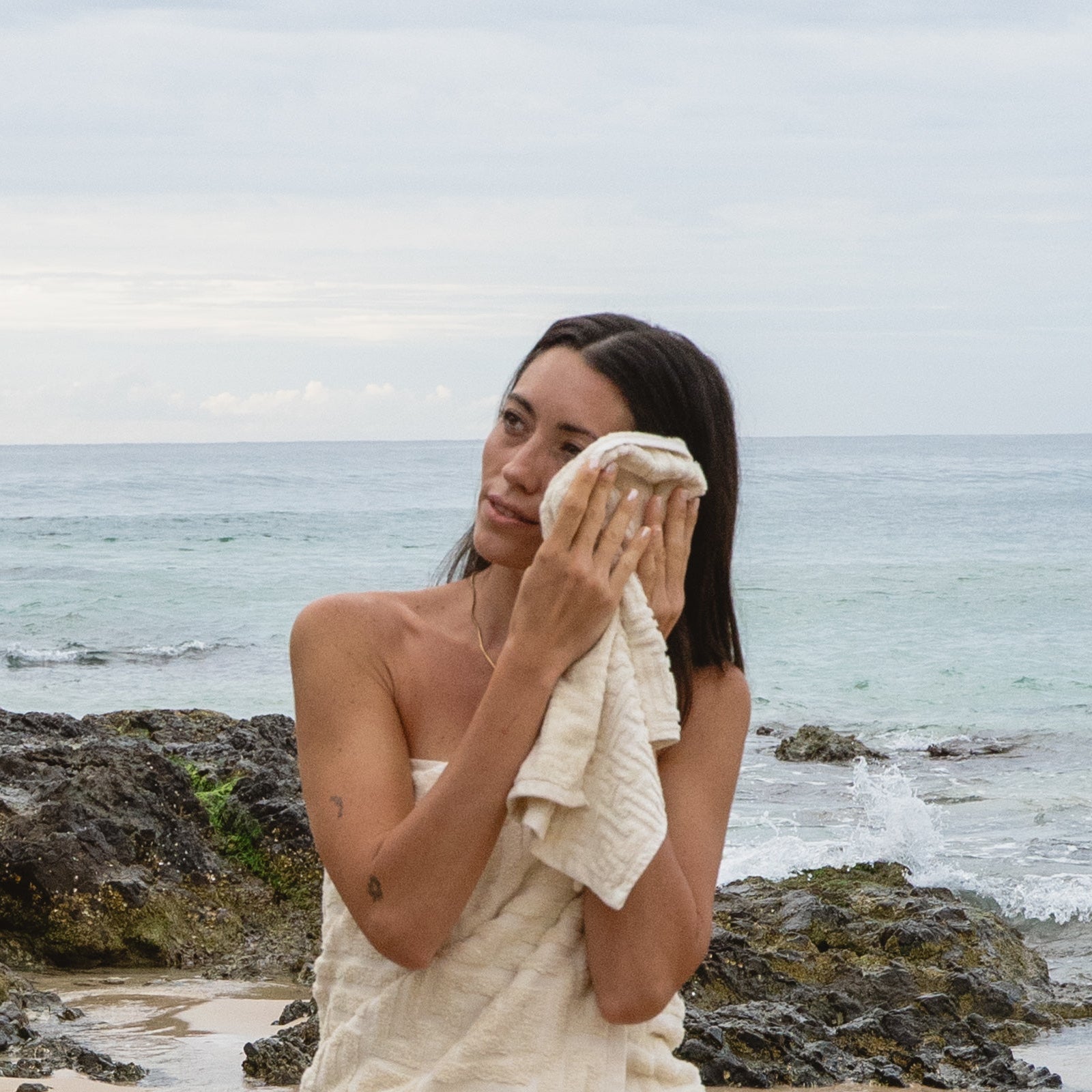 Woman wrapped in a towel on a rocky beach with ocean in the background