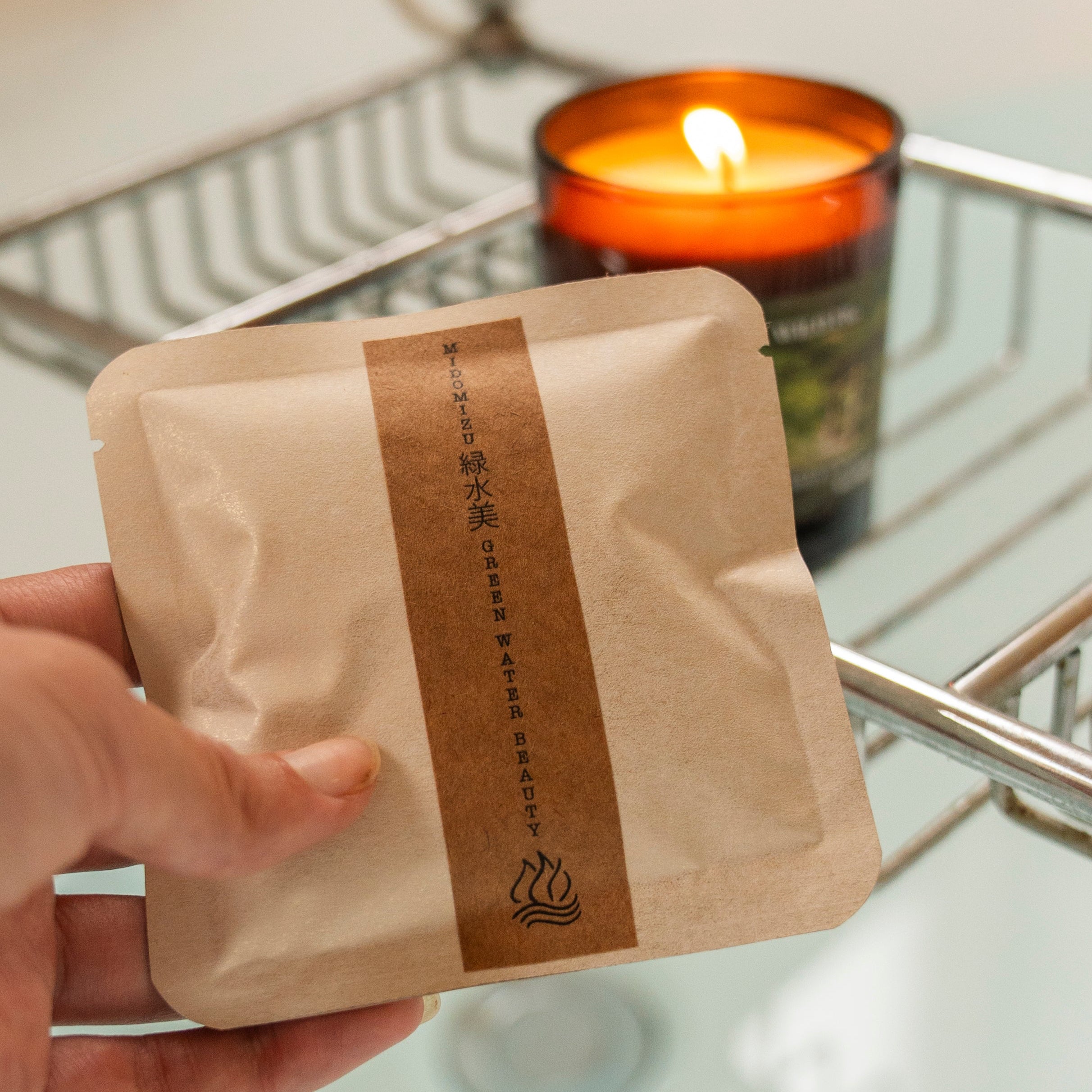 Hand holding a herbal bath soak satchel with a candle in the background