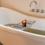 White freestanding bathtub with a metal tray holding a candle, against a beige tiled wall.