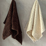 Two textured hand towels in brown, beige, and green hanging on a gray wall.