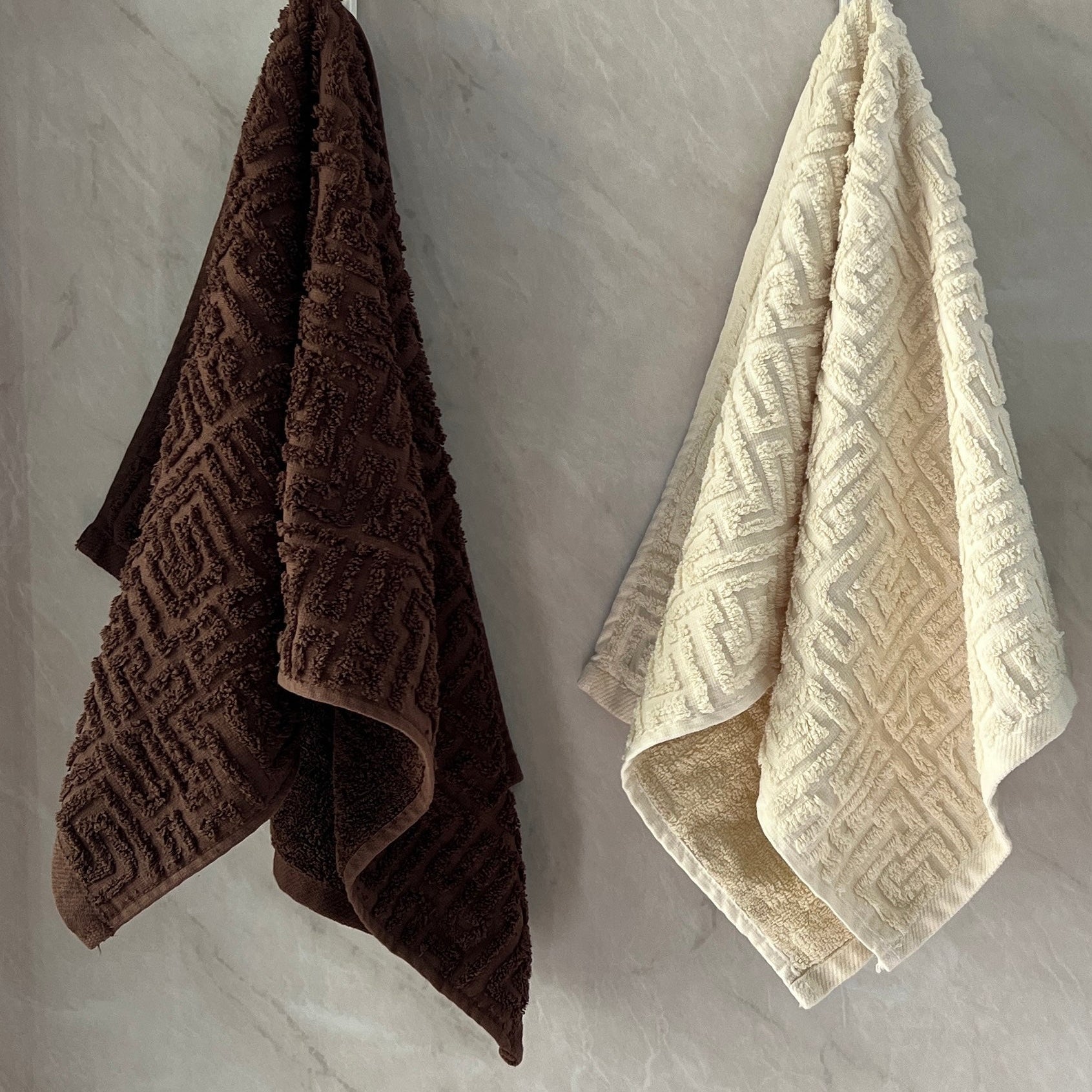 Two textured hand towels in brown, beige, and green hanging on a gray wall.
