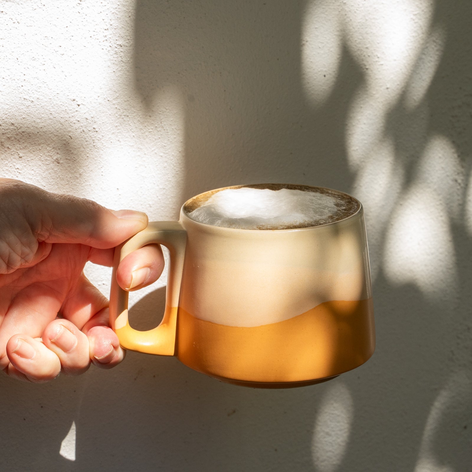 Hand holding a mug of hot liquid against a light background