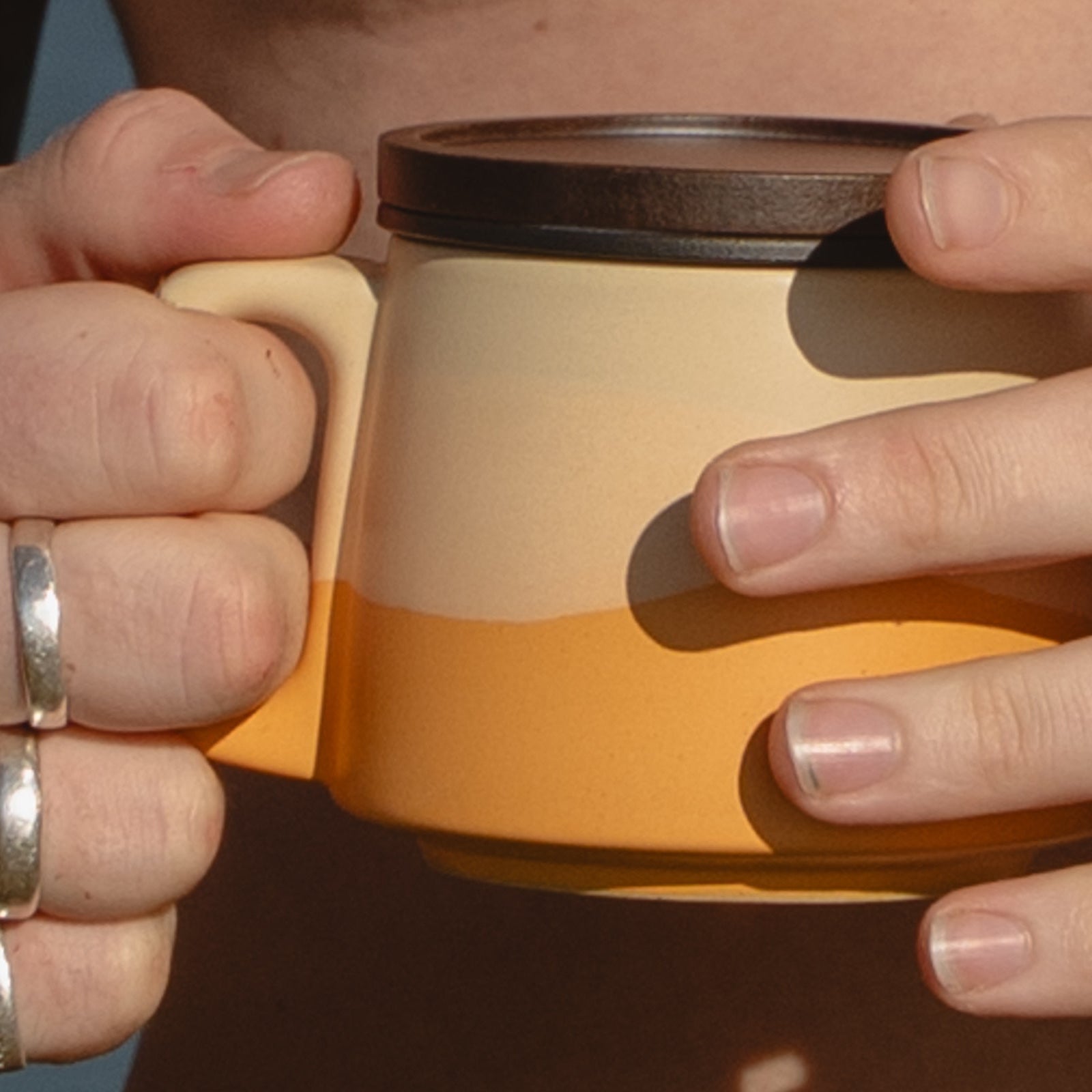 Close-up of hands holding a yellow mug with a black lid.