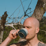 Man with tattoos drinking from a mug outdoors