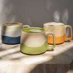 Three ceramic mugs with different color patterns on a wooden surface.