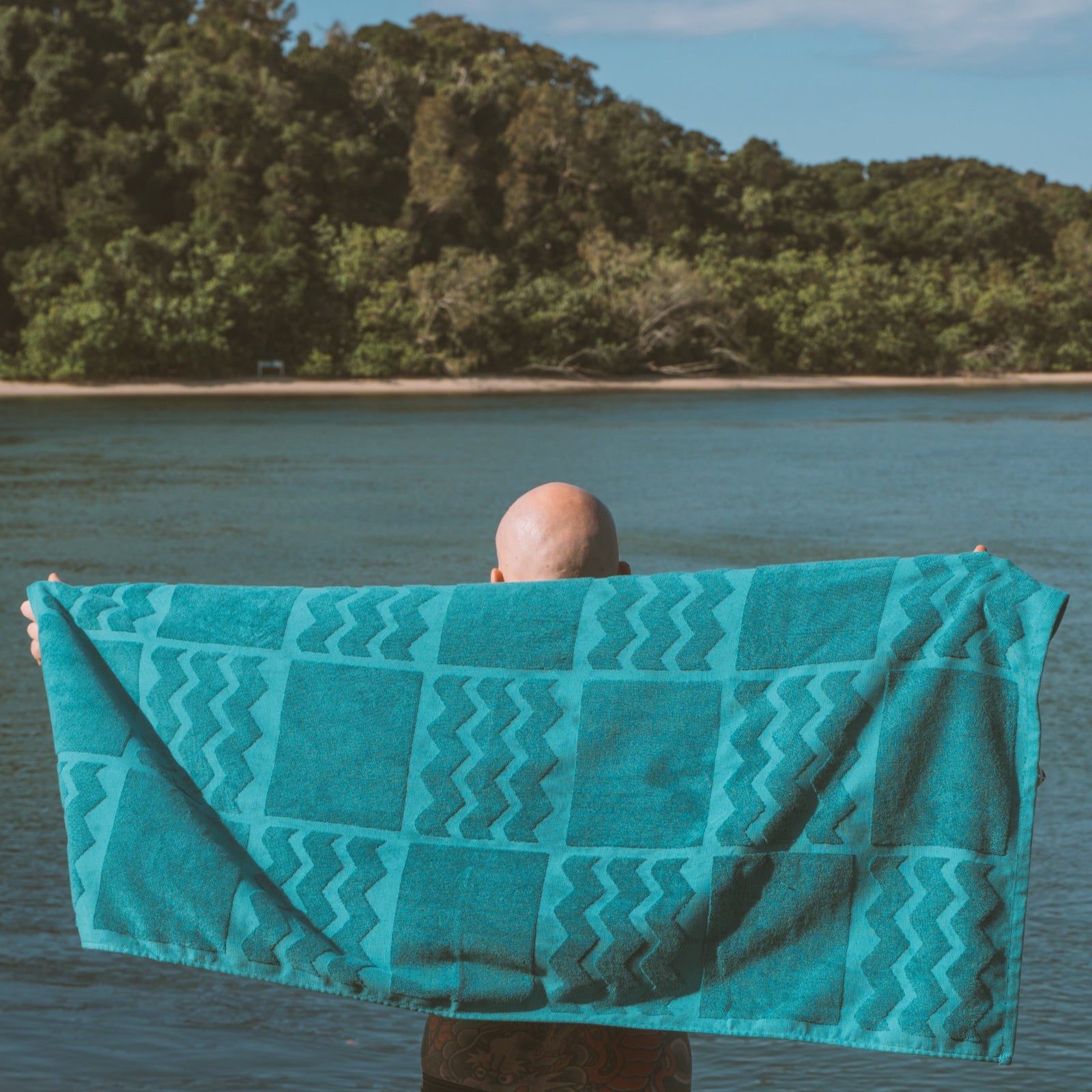 Person holding a teal towel with wavy pattern by a lake
