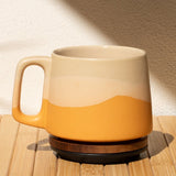 Ceramic mug with a gradient design on a wooden surface with a leaf shadow on the wall.