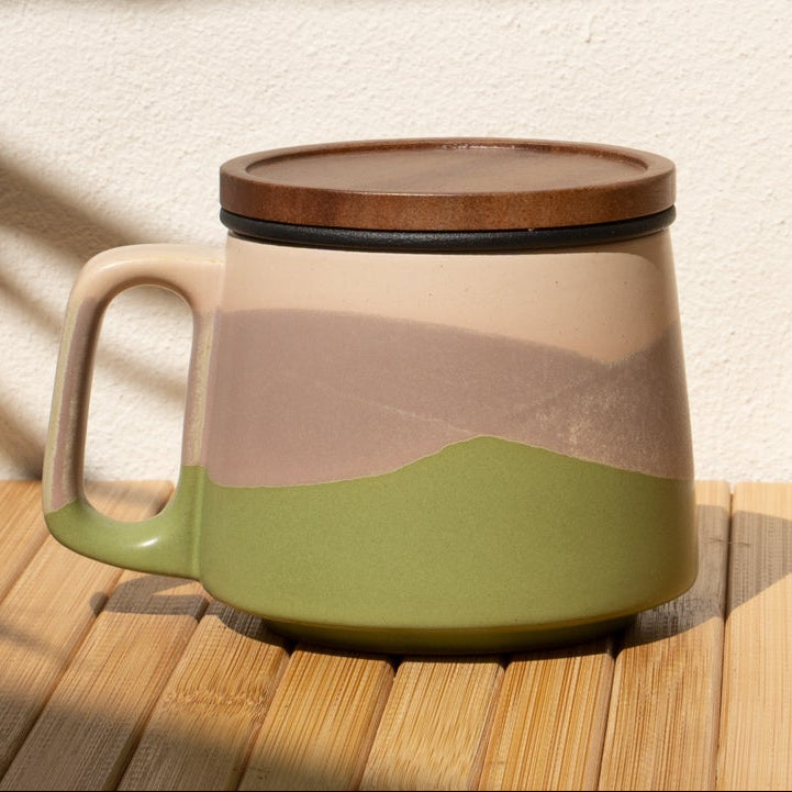 Ceramic mug with a lid on a wooden surface with a shadow of a plant.