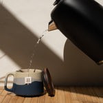Black kettle pouring water into a mug on a wooden surface with a neutral background