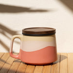 Ceramic mug with a lid on a wooden surface with a shadow of a plant.
