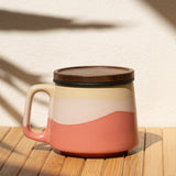 Ceramic mug with a lid on a wooden surface with a shadow of a plant.