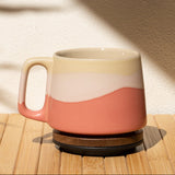 Pink and beige mug on a wooden surface with a shadow of a plant on the wall.