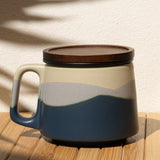 Ceramic mug with a lid on a wooden surface with a shadow of leaves on the wall.