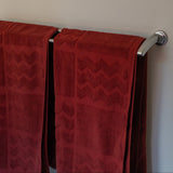 Red towels hanging on a silver towel rack against a beige wall