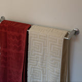 Red and beige patterned towels hanging on a metal towel rack against a beige wall.