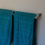 Turquoise towels hanging on a silver towel rack against a white wall.