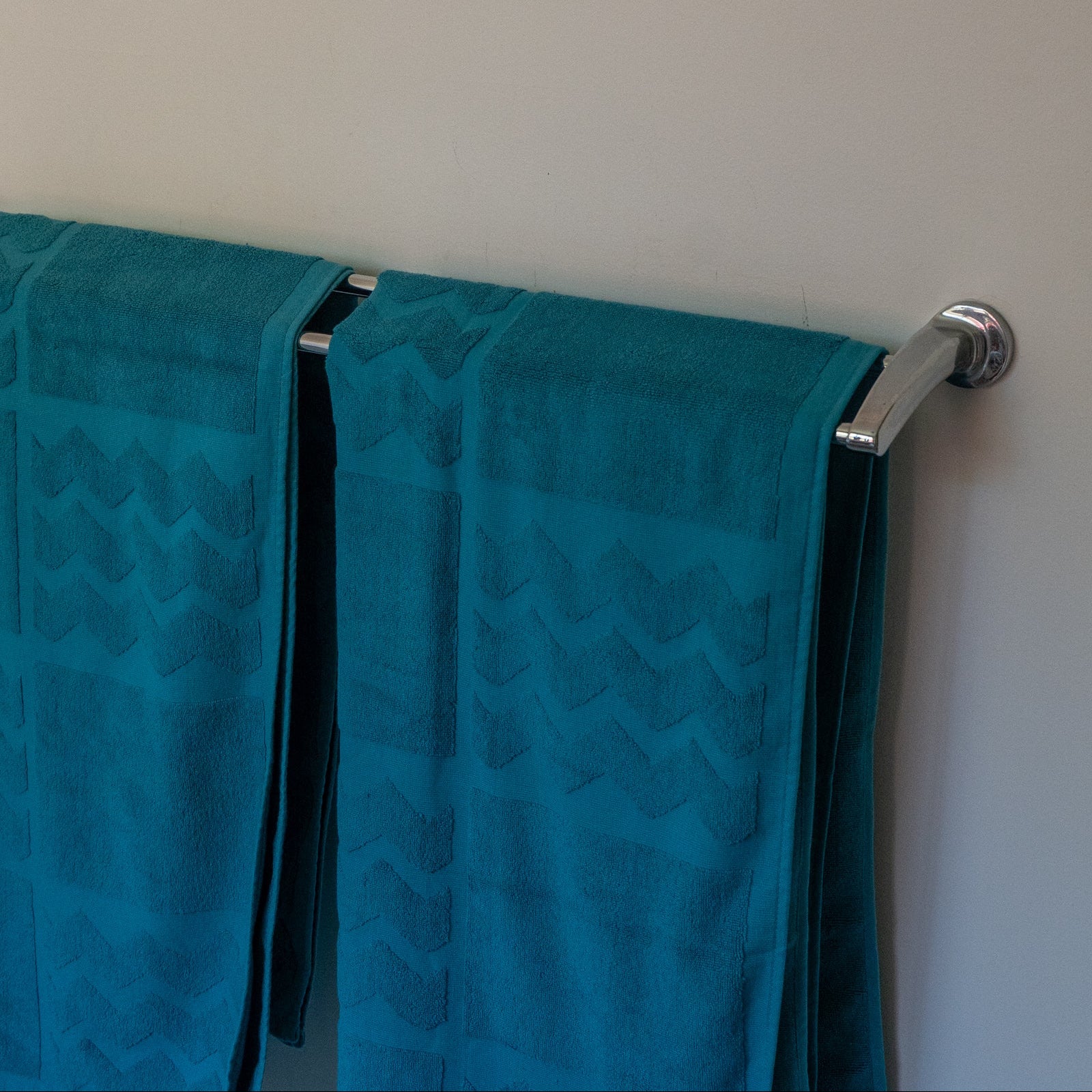 Turquoise towels hanging on a silver towel rack against a white wall.