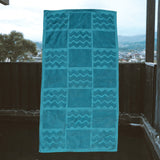 Blue towel with zigzag pattern hanging on a wooden railing with a scenic background.