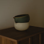 Two ceramic bowls stacked on a wooden surface against a plain wall.