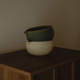 Two ceramic bowls stacked on a wooden surface against a plain wall.