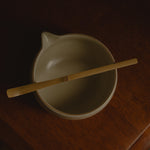White ceramic matcha bowl with a wooden spoon on a dark surface