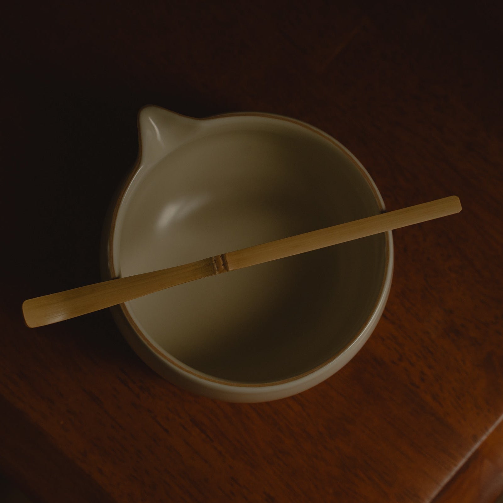 White ceramic matcha bowl with a wooden spoon on a dark surface