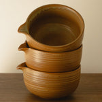 Stack of brown ceramic pitchers on a wooden surface with a beige background