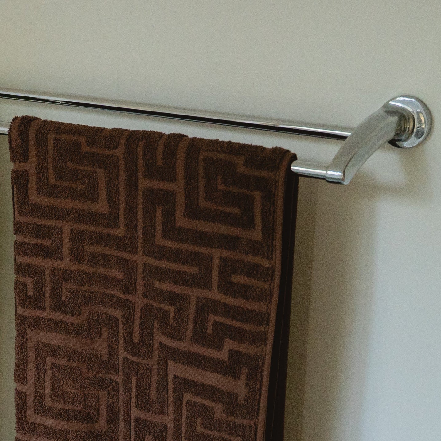 Two patterned towels hanging on a chrome towel rack against a white wall.