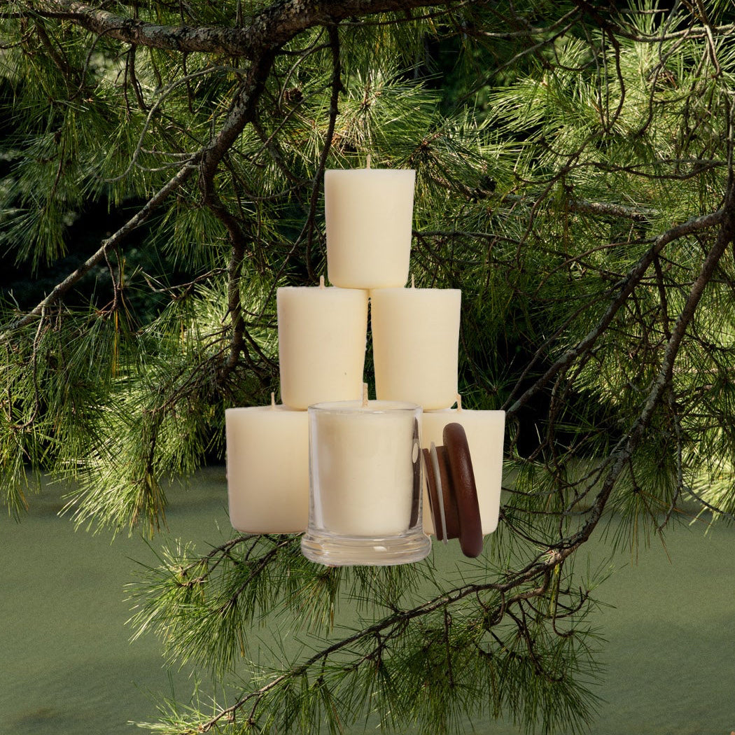 Stack of white candles with a hanging tree branch over water.