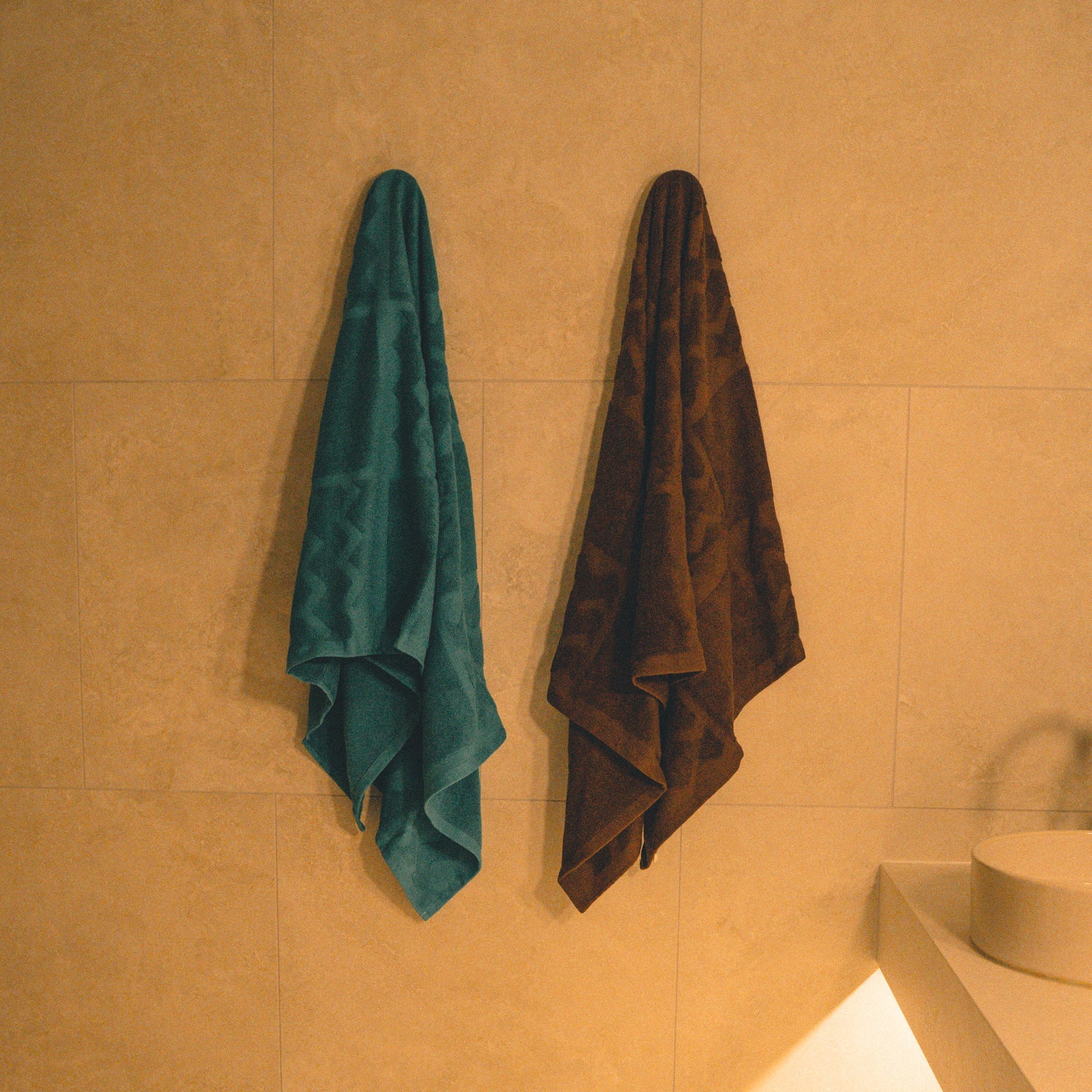 Two towels hanging on a tiled wall in a bathroom.