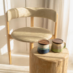 Wooden chair with a small wooden table holding two ceramic mugs against a light curtain background