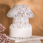 Mushroom candle lamp with white spots on clear glass. Filled with 100% soy wax on tile with dried flowers and tan background.