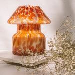 Mushroom candle lamp with red, orange and white spots on clear glass. Retro lamp is filled with 100% soy wax placed one white tiles with dried flowers.