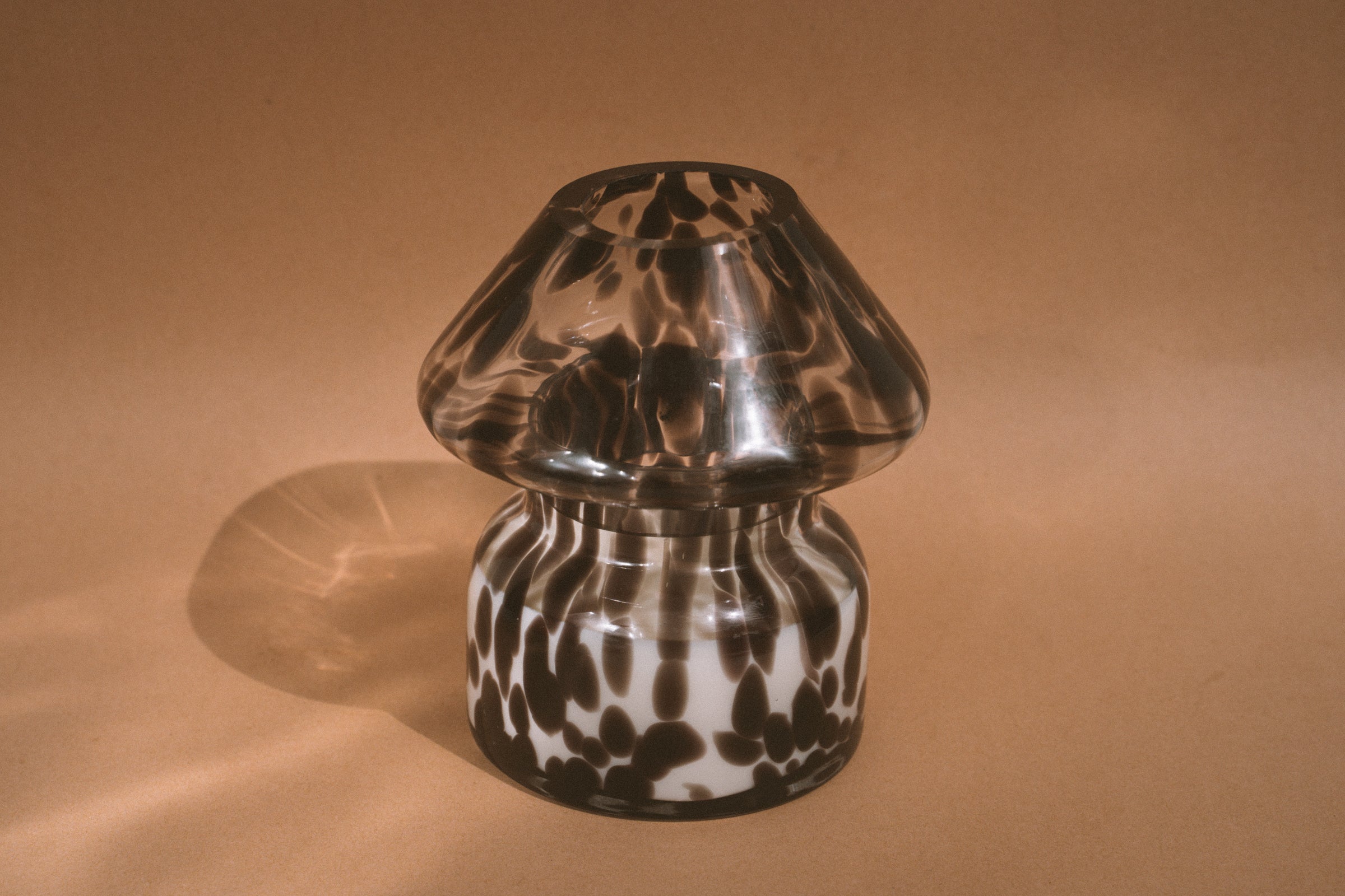 Dalmation spotted black glass mushroom candle lamp. Filled with 100% soy wax on tan background with sun reflection.