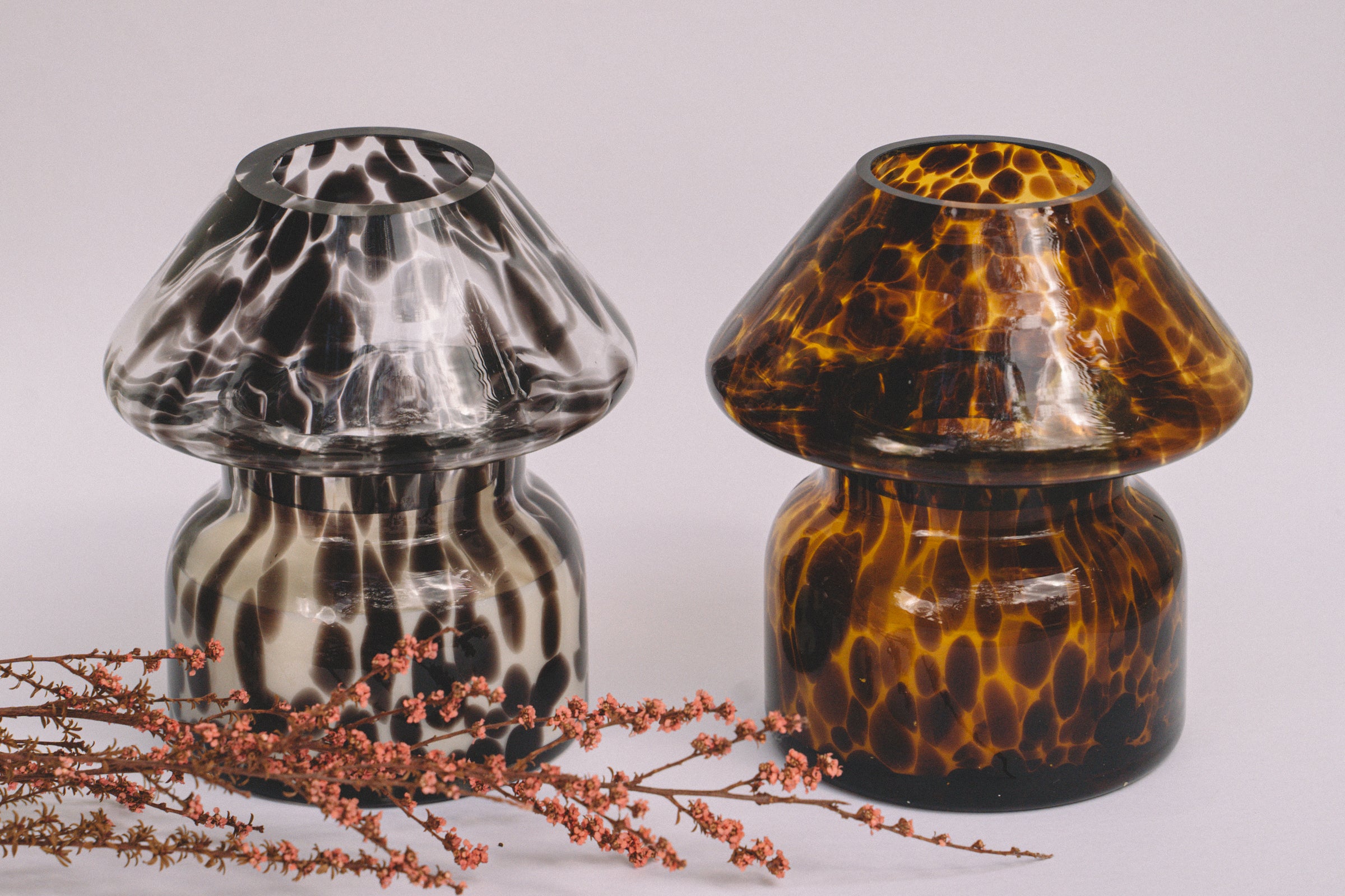 Mushroom candle lamp with black spots on clear glass next to leopard print candle lamp. Filled with 100% soy wax with dried flowers.