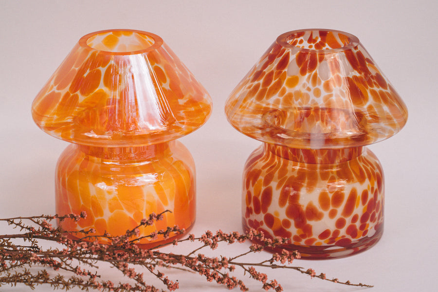 Mushroom candle lamp with light and dark orange spots on clear glass with opal tint next to retro coloured candle lamp. Filled with 100% soy wax.