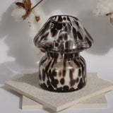Dalmation spotted black glass mushroom candle lamp. Candle lamp is sitting on tile with cotton in the background 