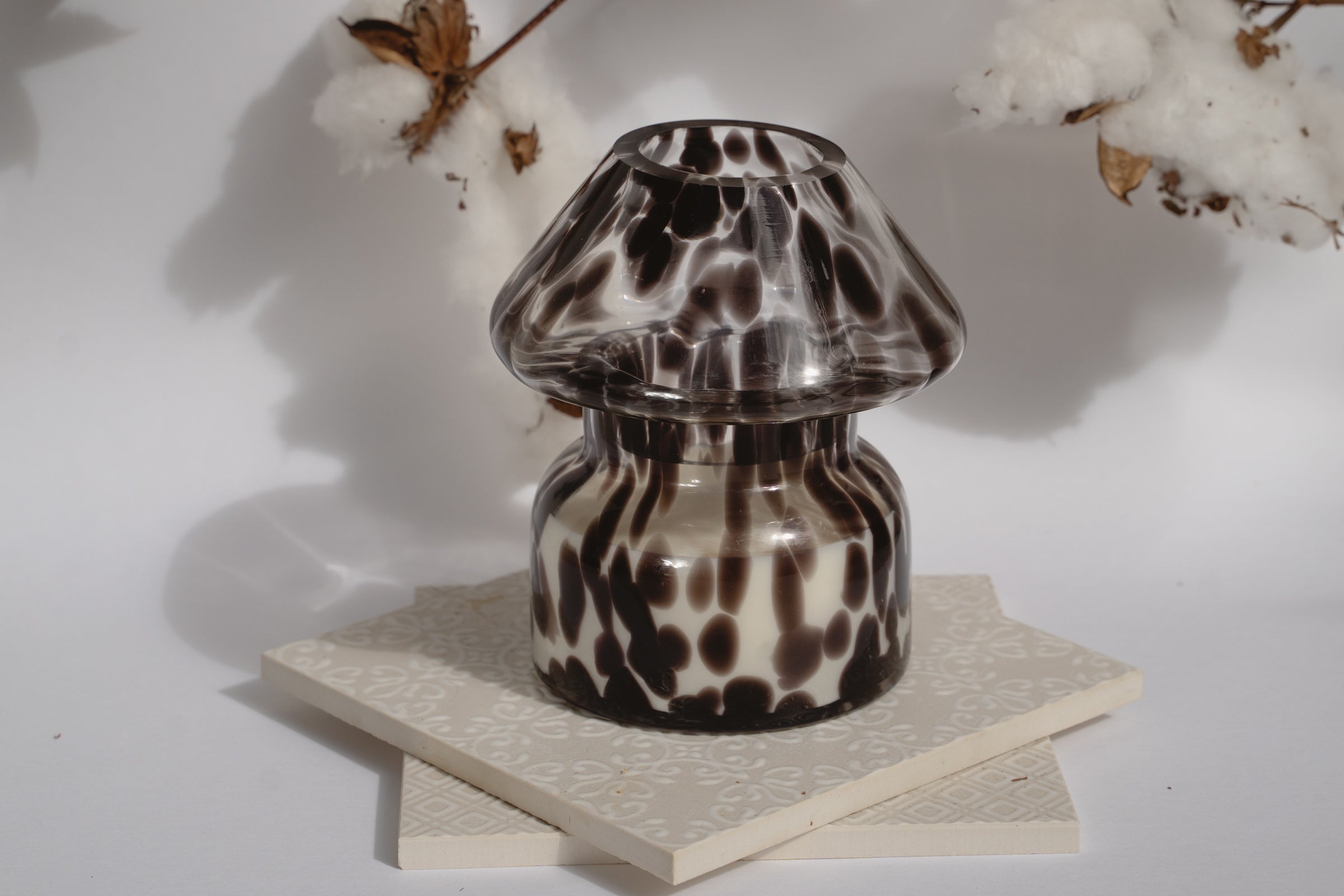 Dalmation spotted black glass mushroom candle lamp. Candle lamp is sitting on tile with cotton in the background 