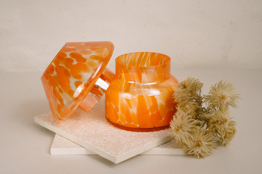 Mushroom candle lamp with light and dark orange spots on clear glass with opal tint and lid ajar. Filled with 100% soy wax.