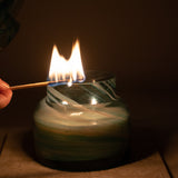 Mushroom candle lamp with aqua blue and gold glitter swirls on clear glass. Mushroom lamp has lid off and it being lit with match.