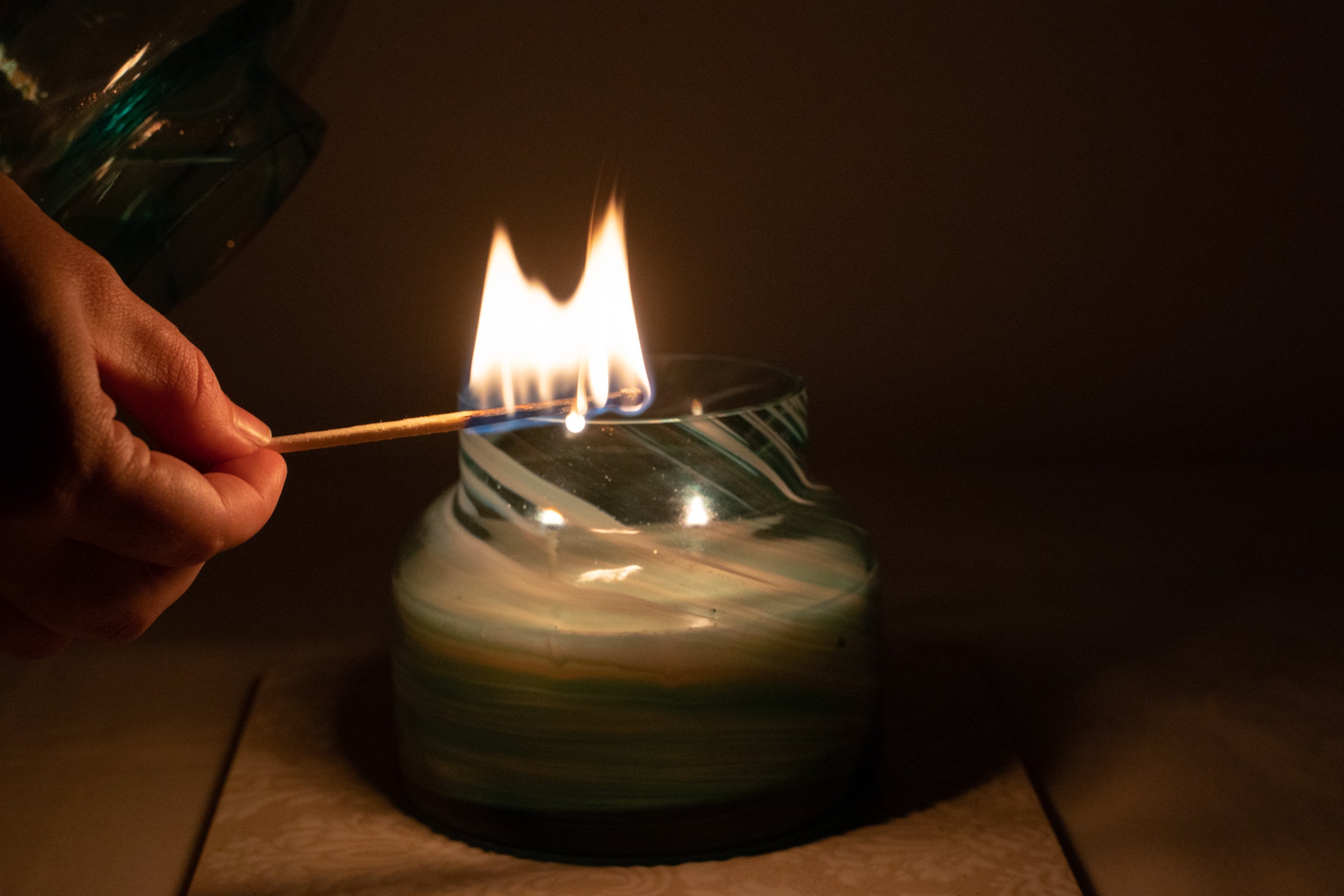 Mushroom candle lamp with aqua blue and gold glitter swirls on clear glass. Mushroom lamp has lid off and it being lit with match.